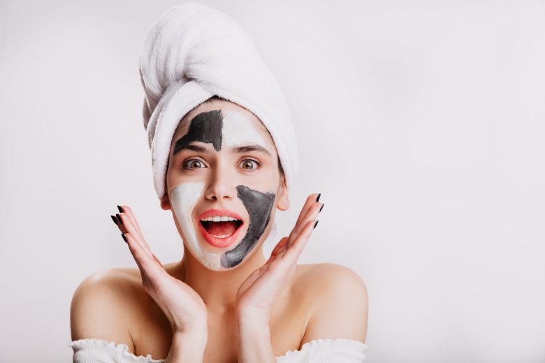 Joyful girl with face mask looks at camera in surprise. Green-eyed woman posing on white background after washing her hair